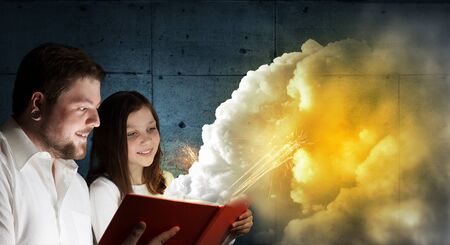 Young father and daughter read book and light coming out of pages