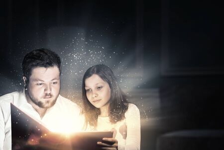 Young father and daughter read book and light coming out of pagesの写真素材