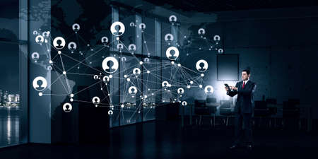 Adult businessman in office dark interior using tablet pcの写真素材