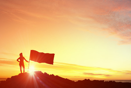 Silhouette of young woman with flag on mountain topの写真素材