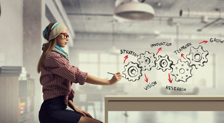 Hipster girl sitting at table and drawing her plan with pencilの写真素材