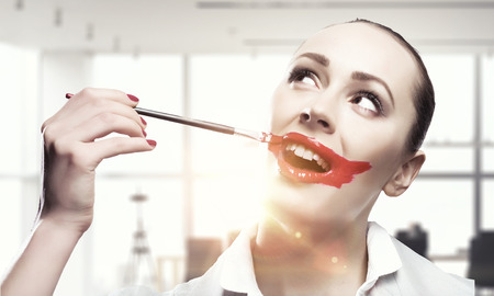 Attractive woman applying red lipstick with brushの写真素材