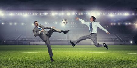 Young businessman in suit playing football at stadiumの写真素材