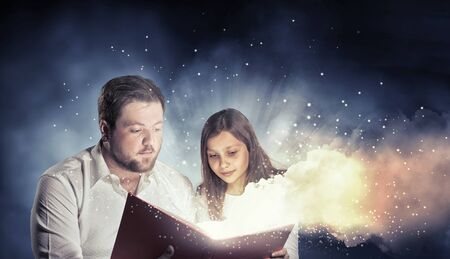 Young father and daughter read book and light coming out of pagesの写真素材