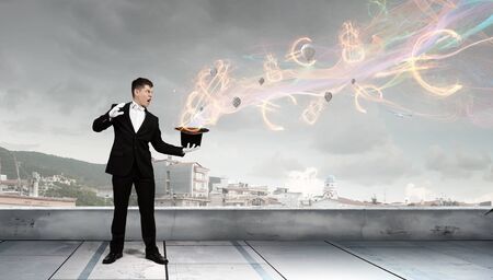 Young cheerful businessman making tricks with magic hat
