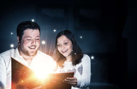Young father and daughter read book and light coming out of pages
