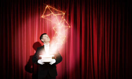 Young cheerful businessman making tricks with magic hatの写真素材