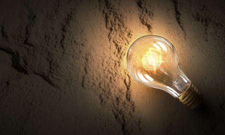 Power and energy concept with glass glowing light bulb on concrete backdropの写真素材