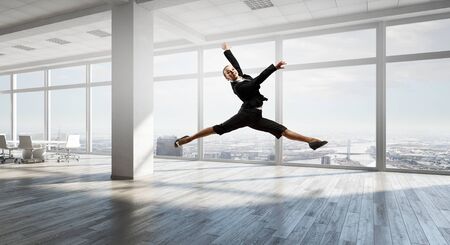 Young dancing businesswoman in suit in modern interiorの写真素材