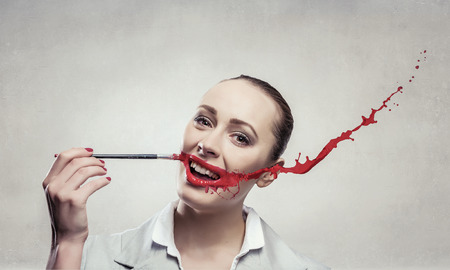 Attractive woman applying red lipstick with brushの写真素材