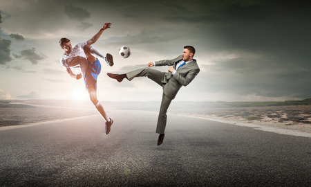 Young businessman in suit playing football outdoorsの写真素材