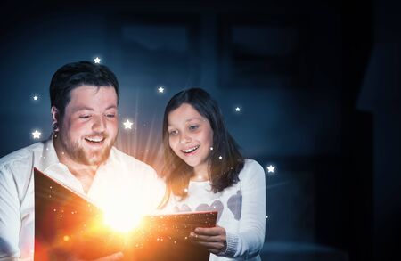 Young father and daughter read book and light coming out of pages