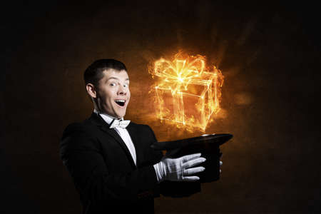 Young cheerful businessman making tricks with magic hatの写真素材