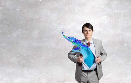 Young businessman acting like super hero and tearing his shirt offの写真素材