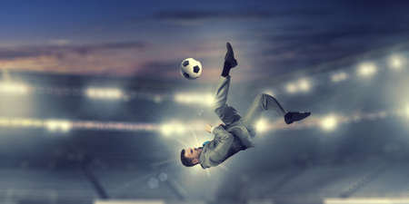 Young businessman in suit playing football at stadiumの写真素材