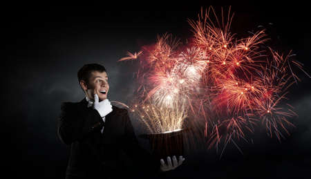 Young cheerful businessman making tricks with magic hatの写真素材