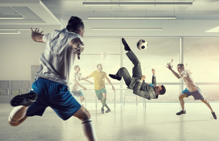 Players and businessman playing soccer ball in modern officeの写真素材