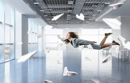 Young careless businesswoman flying in modern office interiorの写真素材