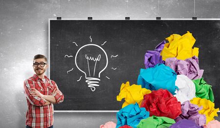 Young man at blackboard and paper balls as symbol of creativityの写真素材