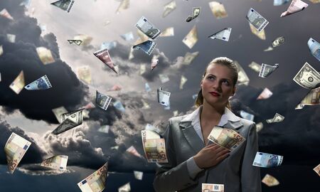 Young businesswoman standing in the rain of money banknotesの写真素材