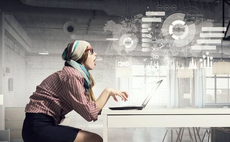 Young hipster girl sitting at table and working on laptopの写真素材