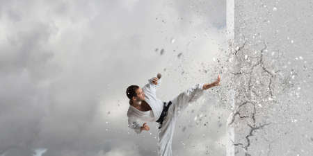 Young determined karate man breaking with leg concrete wallの写真素材