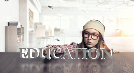 Attractive student girl in red glasses peeping from under tableの写真素材