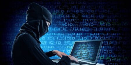 Hacker woman in dark clothes using laptop against digital backgroundの写真素材