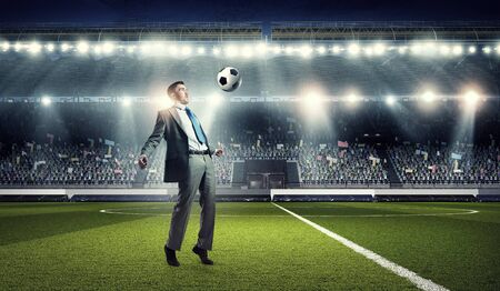 Young businessman in suit playing football at stadiumの写真素材