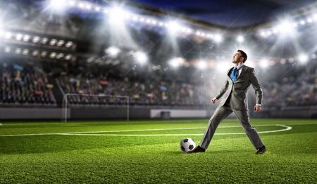 Young businessman in suit playing football at stadiumの写真素材