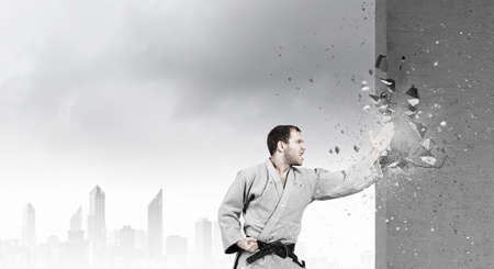 Young determined karate man breaking with leg concrete wallの写真素材