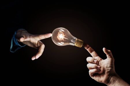 Close up of human hands touching with finger light bulb