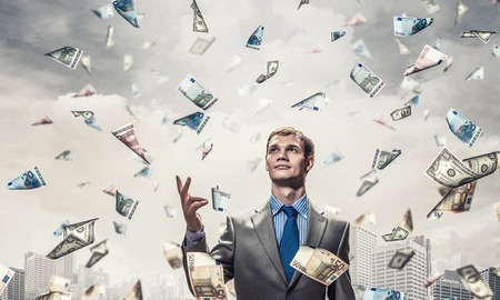 Young businessman standing in the rain of money banknotesの写真素材