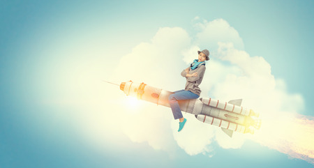 Young cheerful girl riding on rocket high in skyの写真素材