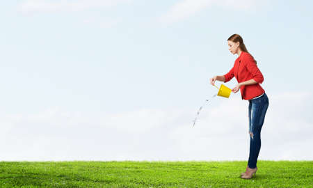Young woman in red jacket holding yellow bucket in handsの写真素材