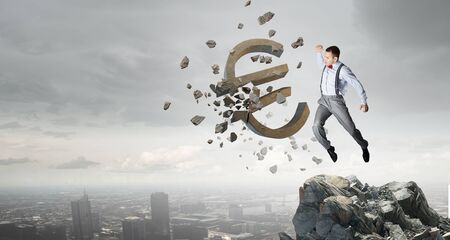 Determined businessman in anger breaking stone euro signの写真素材