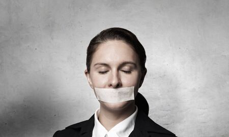 Young businesswoman with tape on mouth and tired handsの写真素材