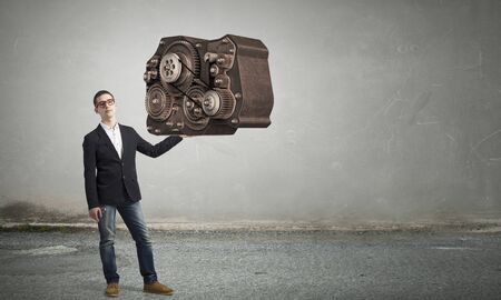 Young student guy in jacket and jeans and gears mechanism as collaboration conceptの写真素材