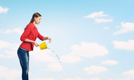 Young woman in red jacket holding yellow bucket in handsの写真素材