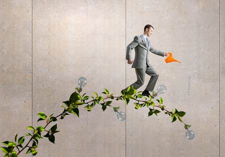 Young businessman watering green plant with canの写真素材