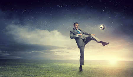 Young businessman in suit playing football outdoorsの写真素材