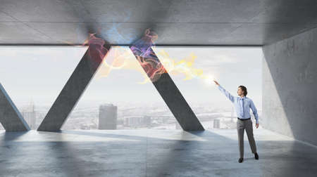 Businessman in building interior reaching hand to touch lightの写真素材