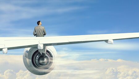 Young businessman sitting on wing of airplane and reading book