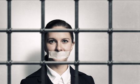 Young businesswoman with tape on mouth and tired handsの写真素材