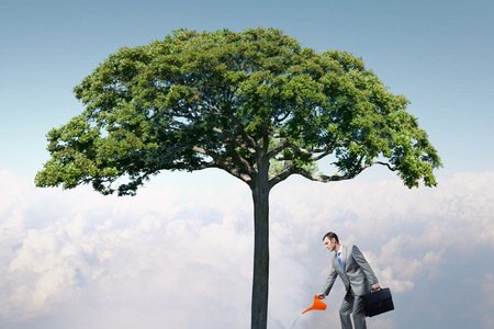 Young businessman watering green plant with canの写真素材
