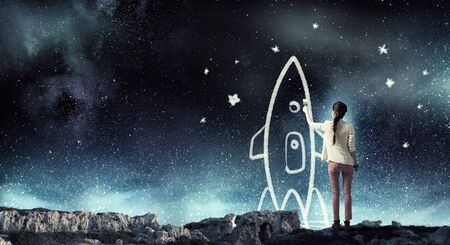 Young student girl standing with back and drawing rocketの写真素材