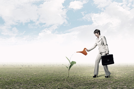 Young businesswoman watering green plant with canの写真素材