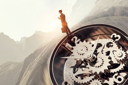 Businessman standing on old clock mechanism against sky background