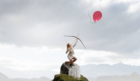 Young businesswoman aiming with archer to make shotの写真素材