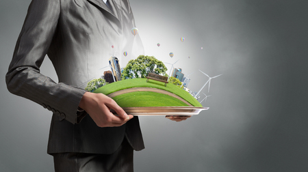 Green eco life of modern city presented in hands of businesswomanの写真素材